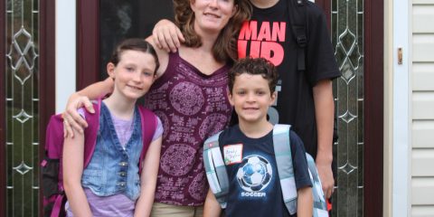 Family of four with backpacks standing at front door, ready for school.