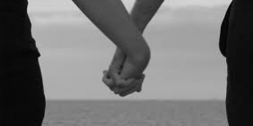 Close-up of two people holding hands by the ocean, symbolizing love and connection.