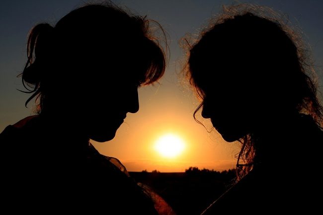 Silhouette of two women facing each other during sunset, creating a peaceful and intimate scene.