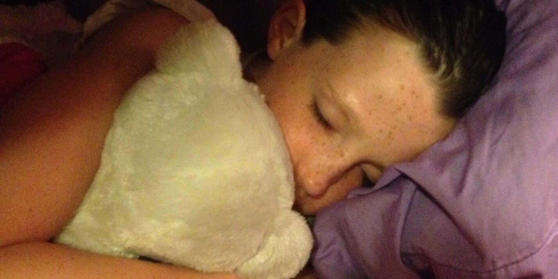 Girl sleeping peacefully with a stuffed animal in a dimly lit room.