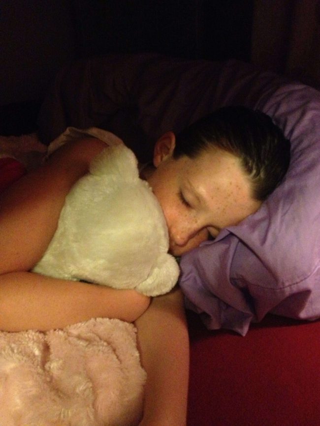 Girl sleeping peacefully with a stuffed animal in a dimly lit room.