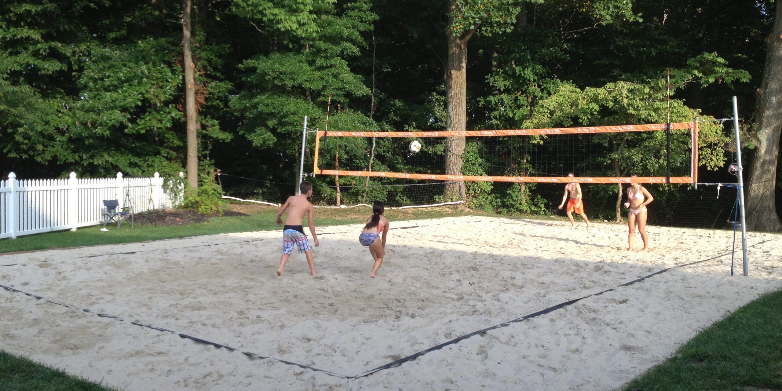 Children playing beach volleyball on sand court outdoors.