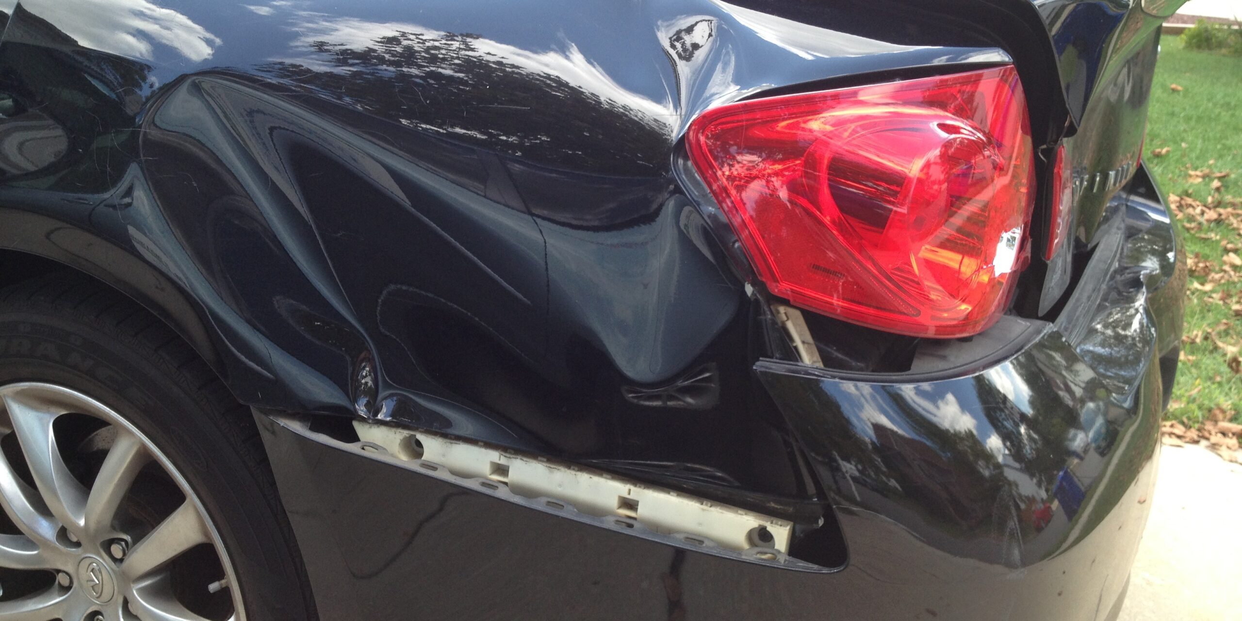 Damaged black car rear with dent and scratches, auto repair service.