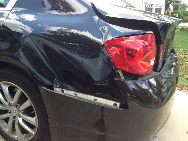 Damaged black car rear with dent and scratches, auto repair service.